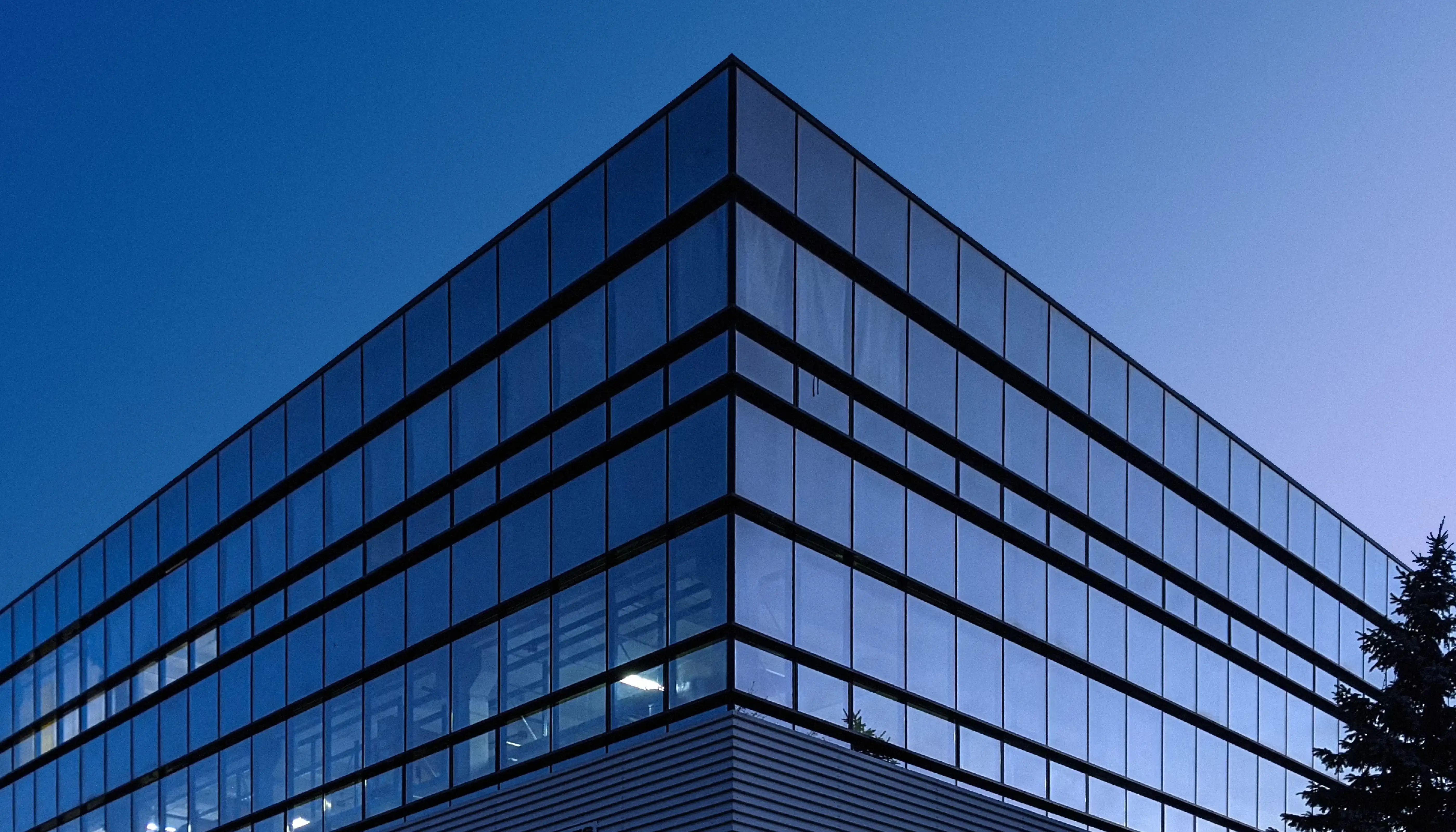 Corner view of a modern blue glass corporate office building under a blue sky.