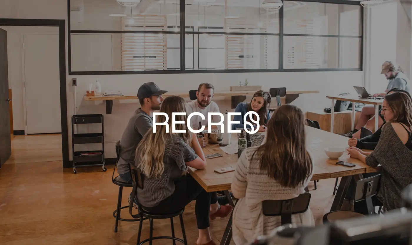 White Recre brand logo overlaid on a photograph of a diverse marketing team having a collaborative meeting at a large wooden table in a modern office.